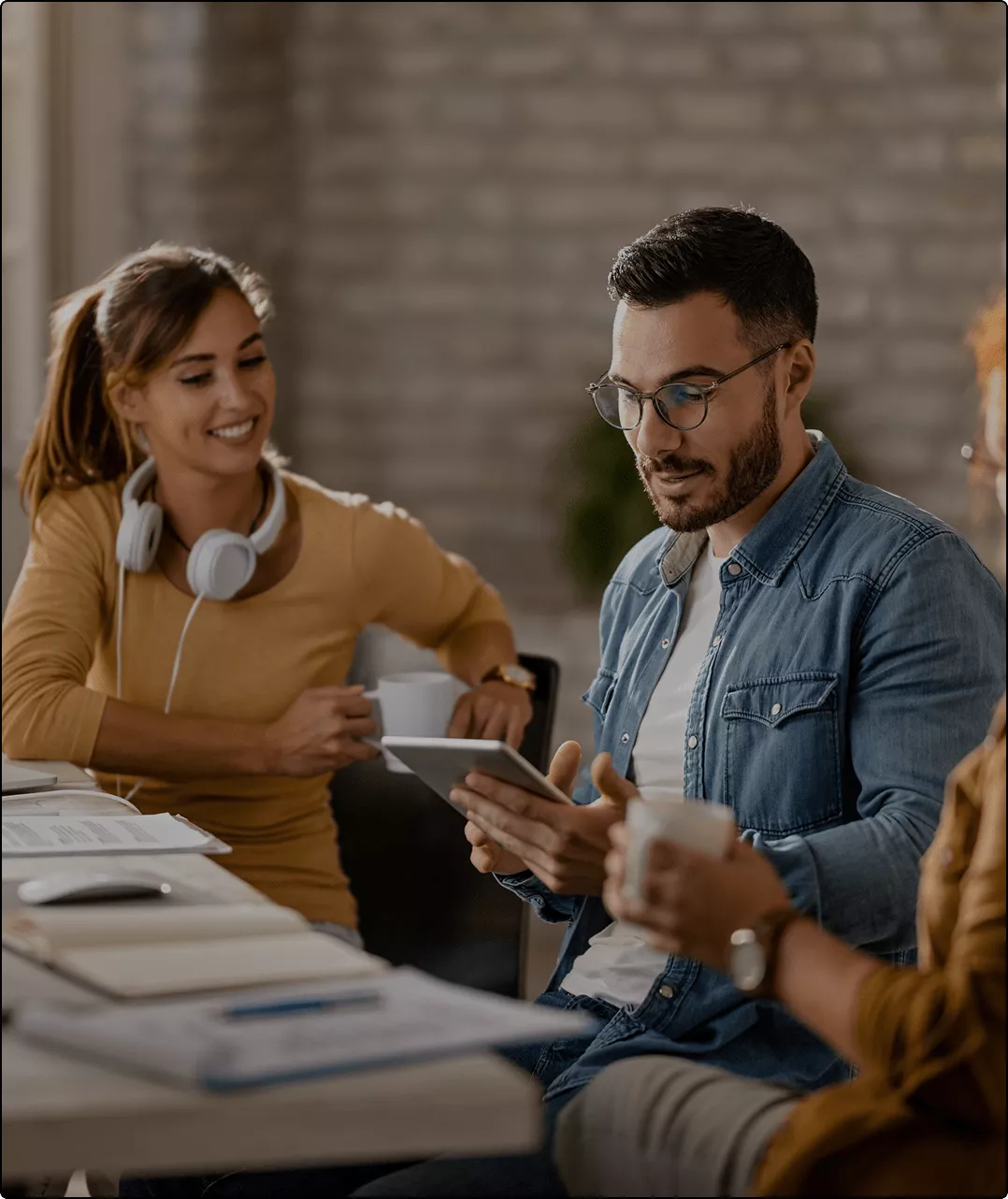 Imagem de uma equipe colaborativa em ambiente de trabalho, com um homem usando tablet e uma mulher sorrindo ao lado, ambos segurando xícaras. A imagem transmite produtividade e conexão em um ambiente moderno de trabalho.
