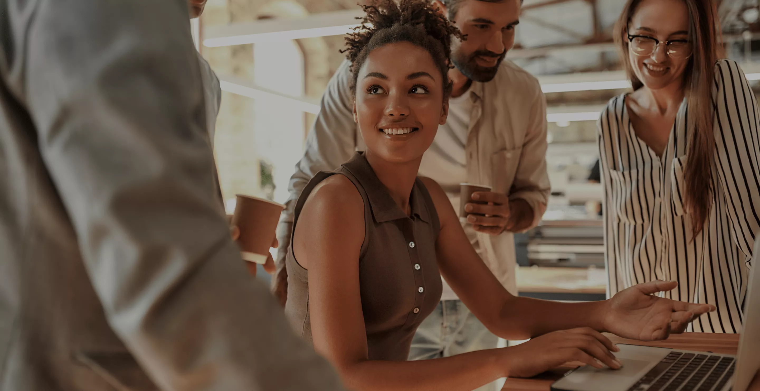 Equipe colaborando em ambiente de trabalho moderno, reunida ao redor de um notebook